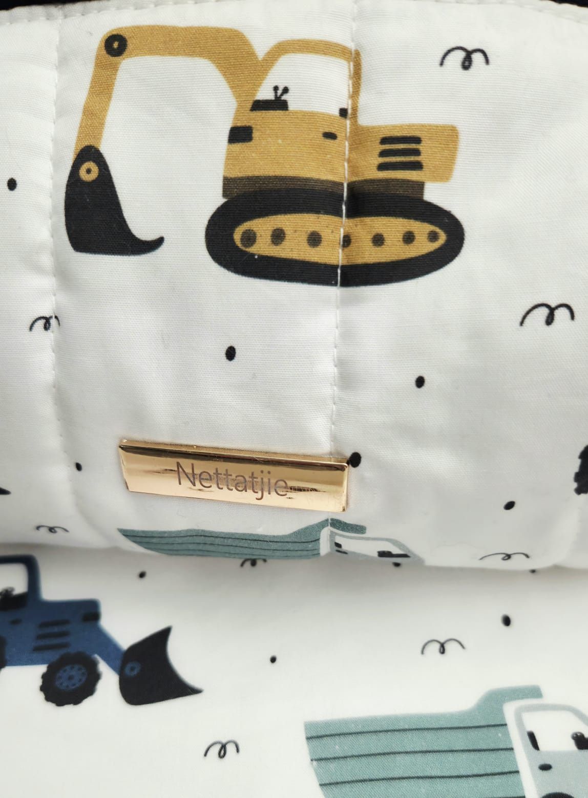 Close-up of Nettatjie branded white fabric with colorful construction vehicles including yellow excavator and blue tractor pattern.