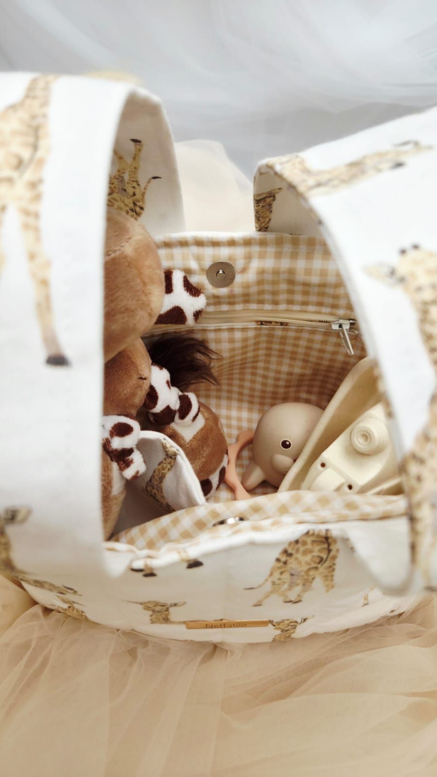 Giraffe-print fabric baby basket with plush toys and a doll nestled inside checkered lining.
