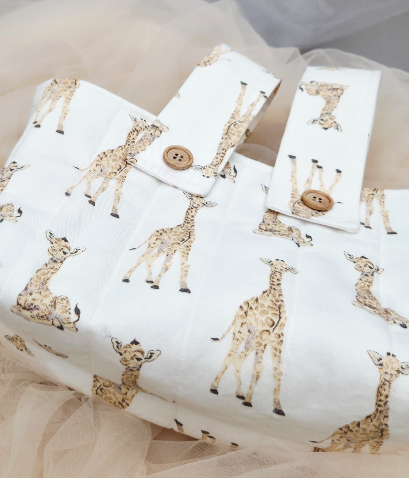 White fabric gift wrap with giraffe print pattern, secured with a wooden button closure.