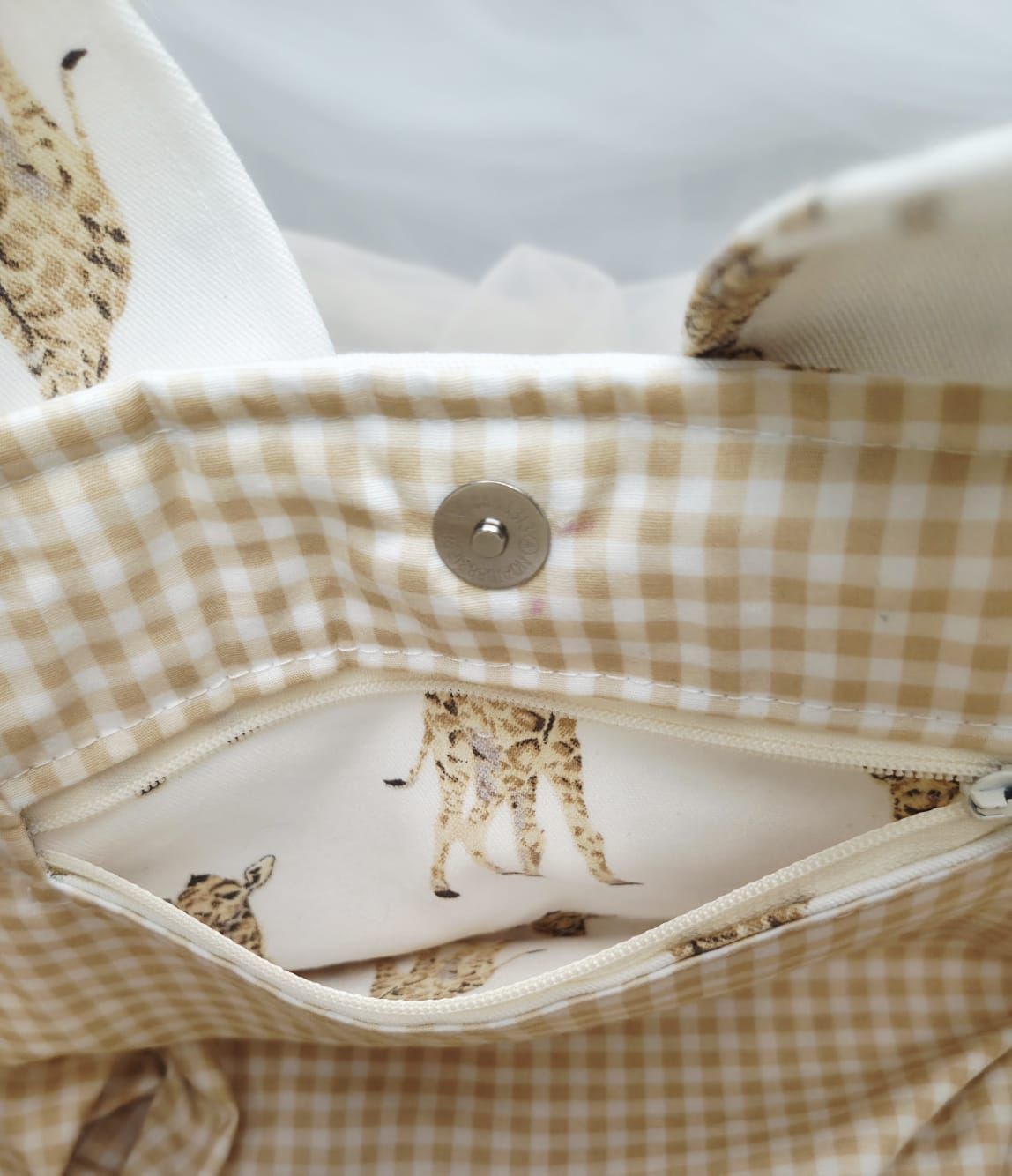 Interior of a fabric bag with beige gingham lining, snap closure, and charming giraffe print pocket detail.
