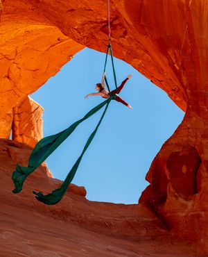 Aerialist on silks framed by a Utah red rock arch; powerful aerial arts image showcasing form, height, and dramatic natural landscape.