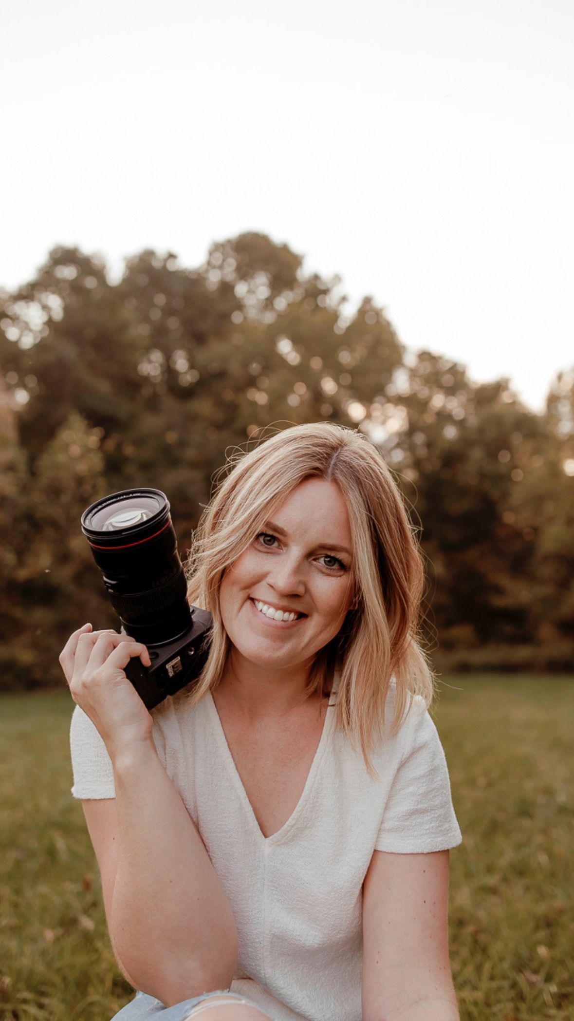 Professional photographer holding a camera lens outdoors during golden hour.