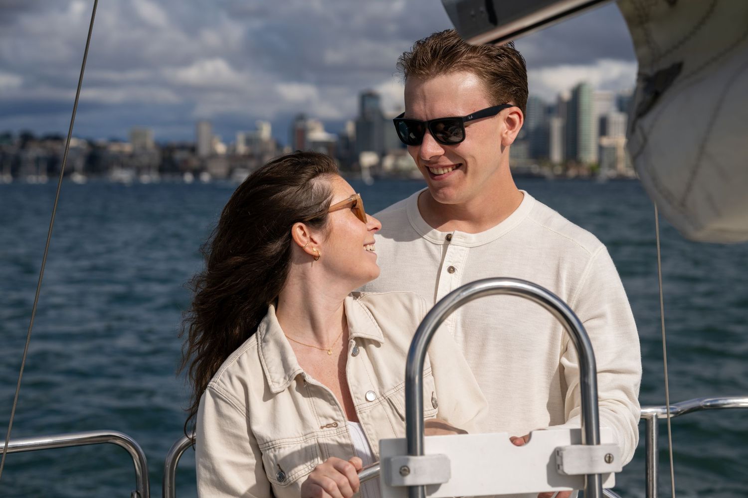 Couples: couple dressed in white stands on a sailboat smiling at each other with the San Diego skyline in the background
