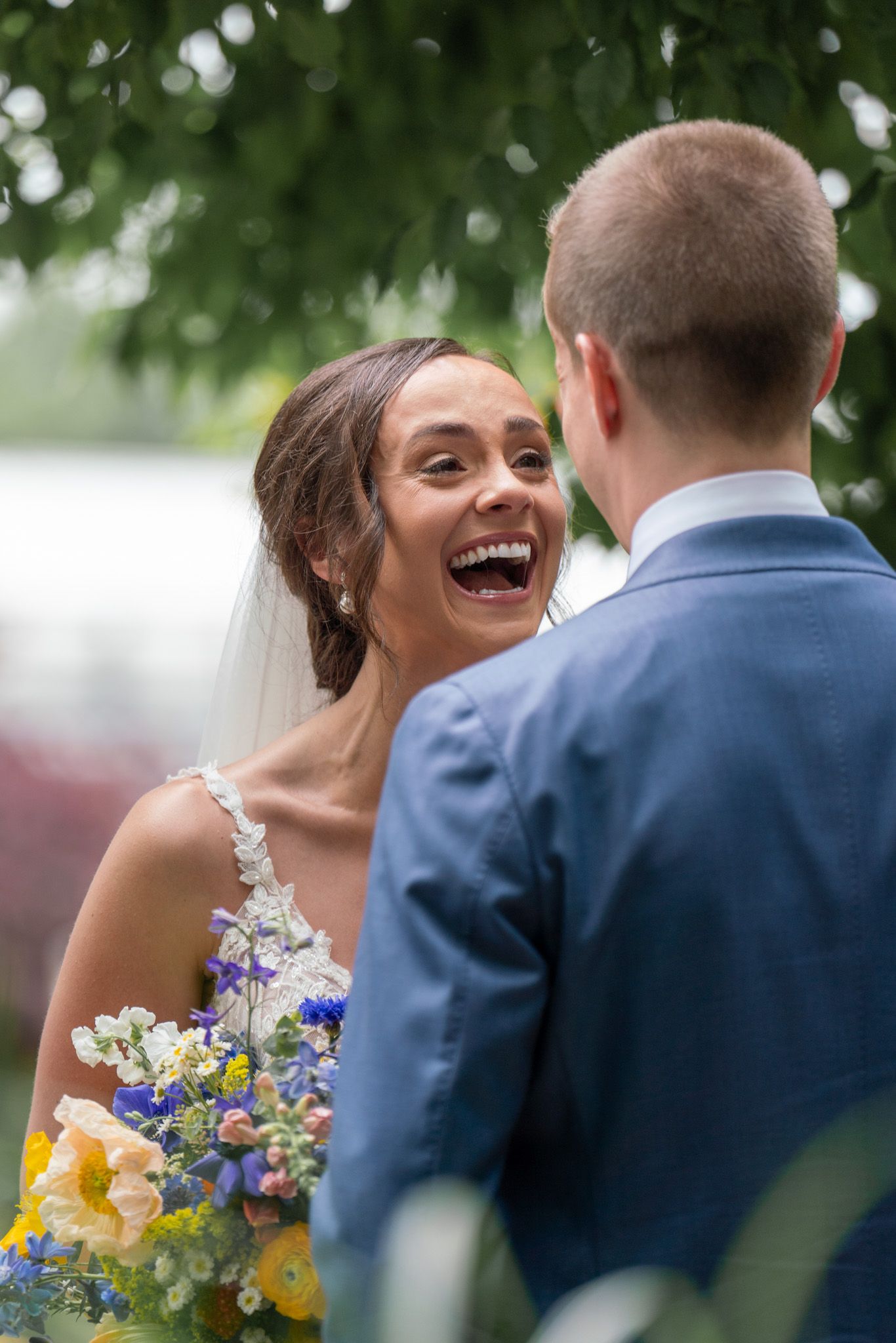 A joyful bride with colorful bouquet laughs during outdoor wedding ceremony.