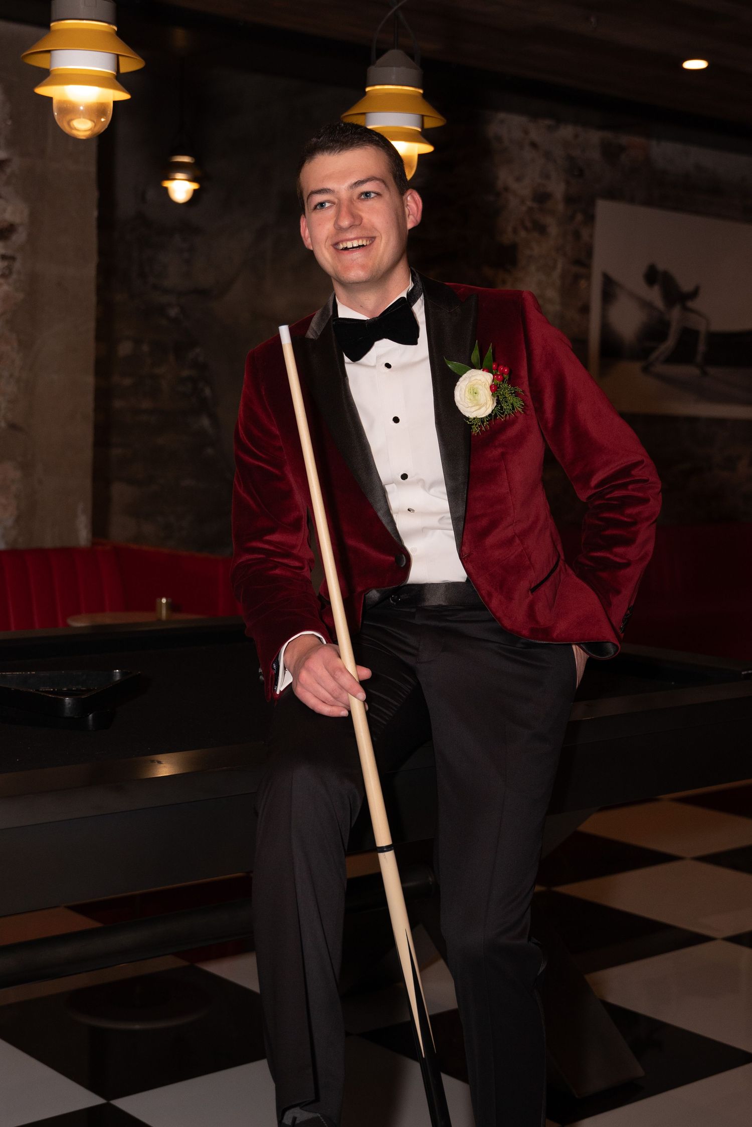 Person in formal red velvet jacket poses with pool cue in vintage-style billiards room.