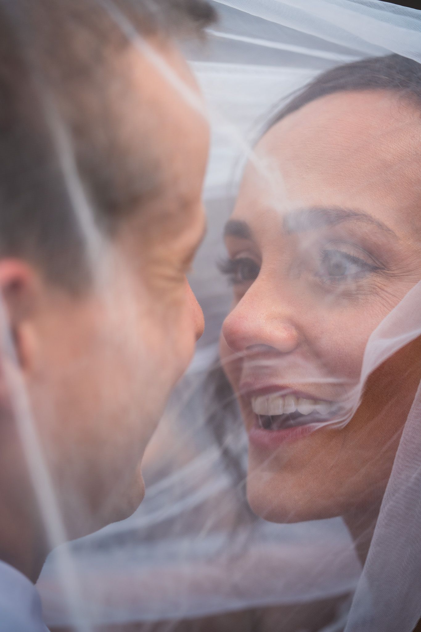 Close-up portrait of joyful couple sharing tender moment under sheer veil.