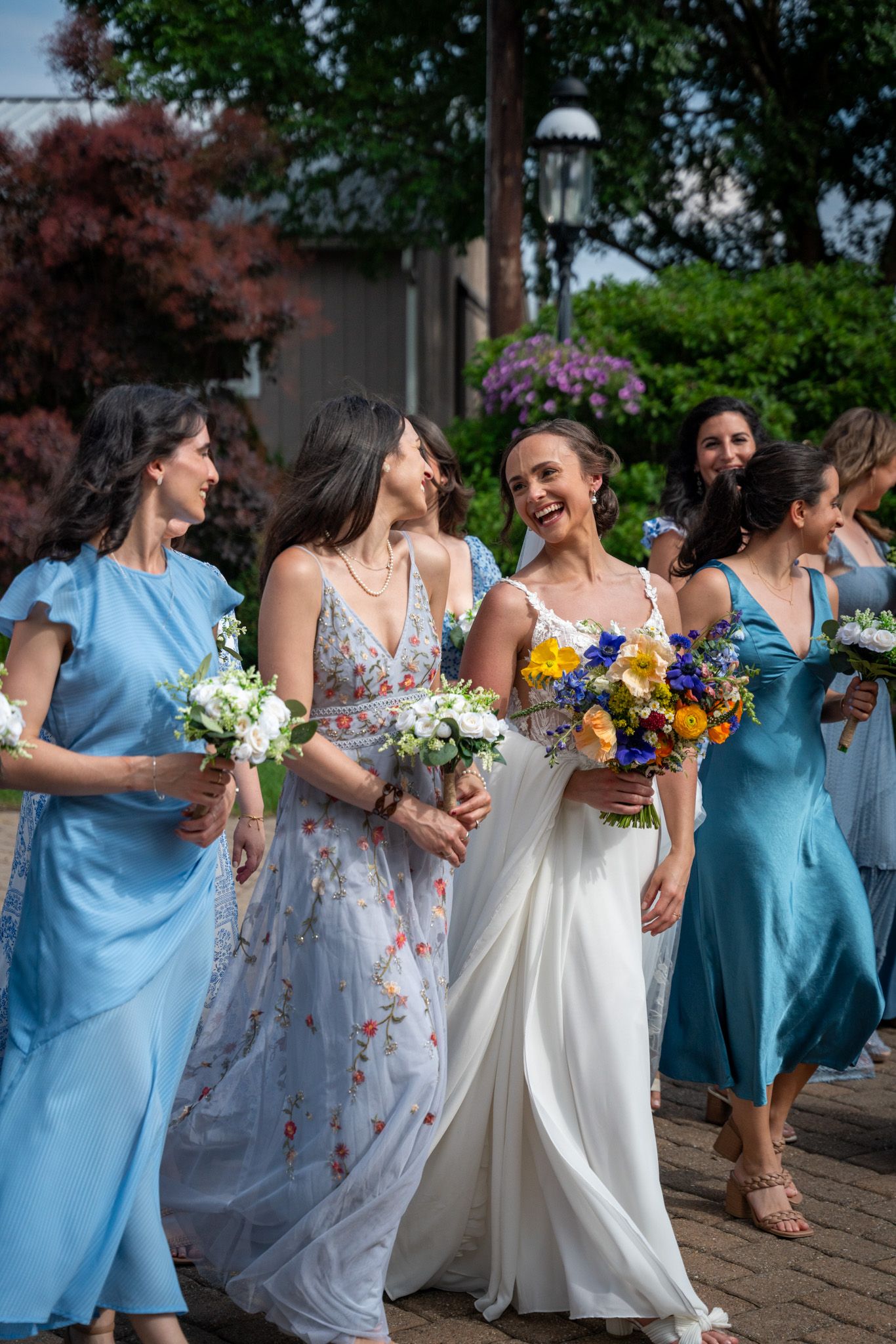 Bridal party in light blue dresses walking together with bouquets outdoors.