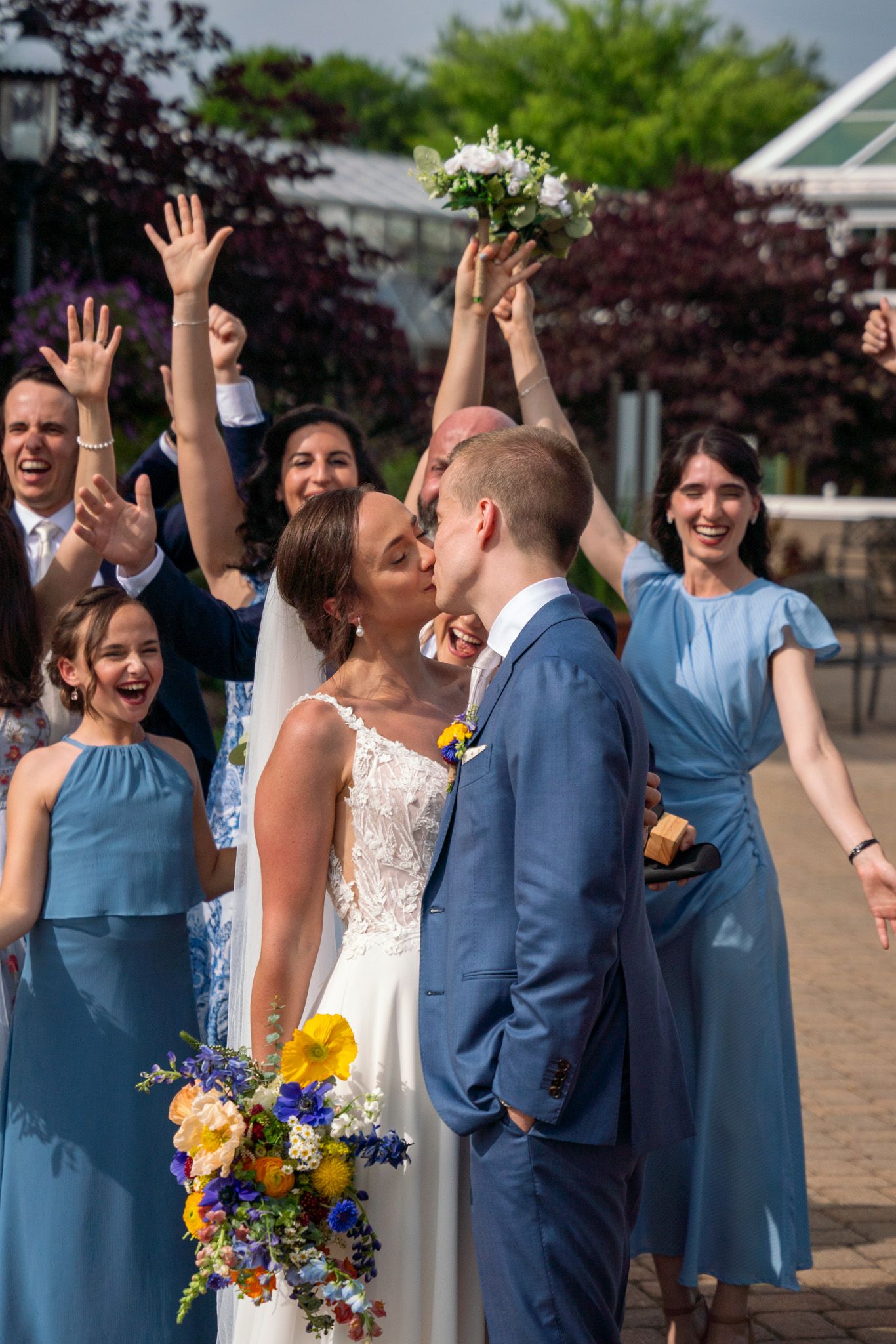 Wedding celebration with bridal party cheering and raising hands outside.