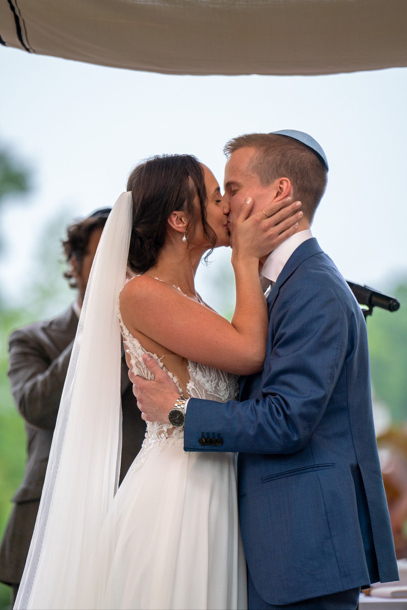 A wedding couple shares their first kiss under a canopy during an outdoor ceremony.