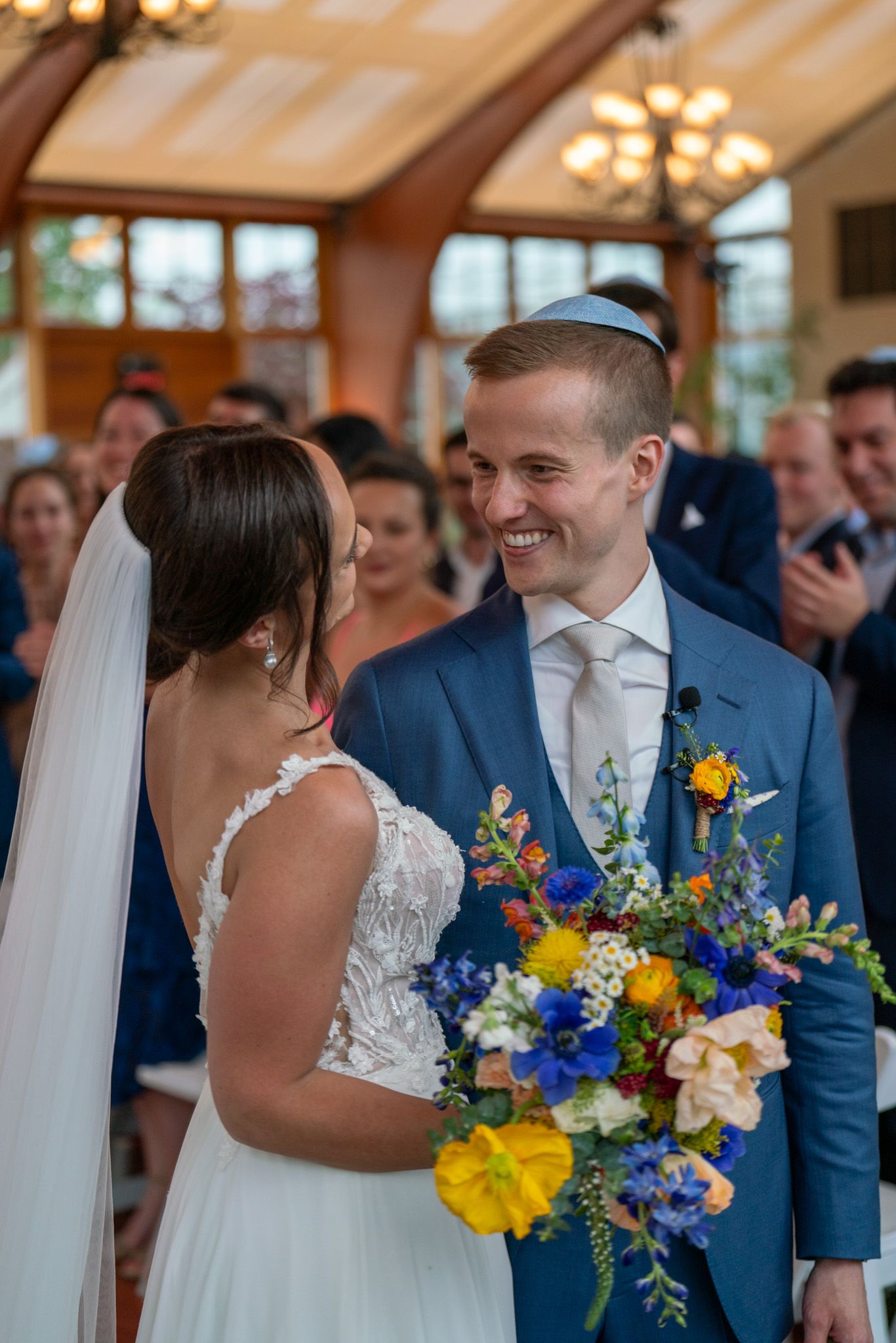 Indoor wedding ceremony moment with bright floral bouquet and natural lighting.