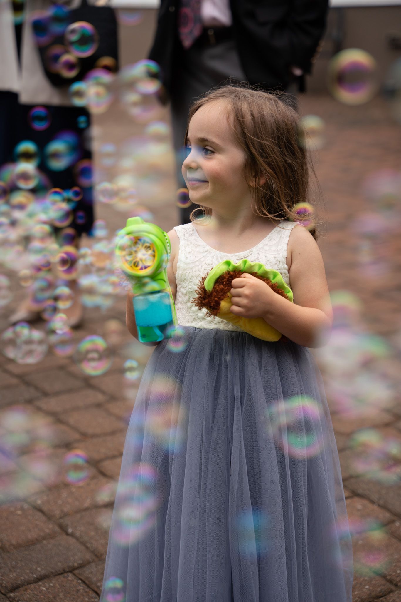 Young flower girl in a tulle dress plays with bubbles during wedding celebration.