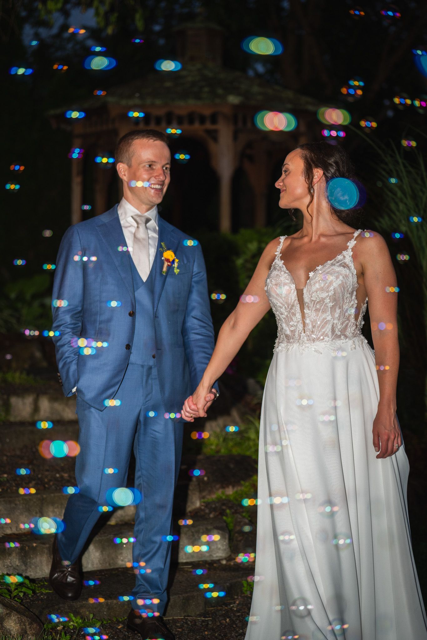 Couple in wedding attire poses together while surrounded by illuminated bokeh lights.