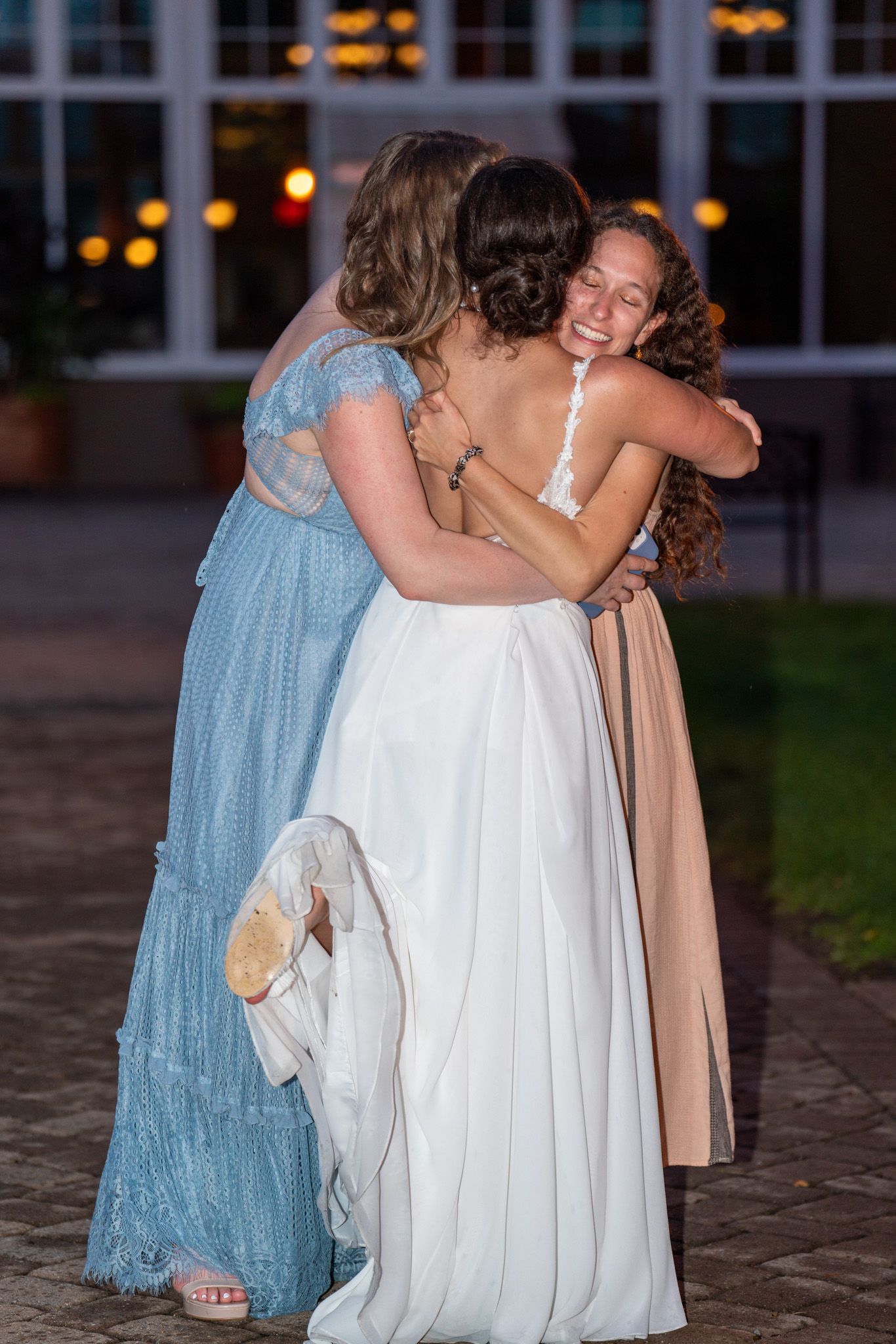 Wedding guests share emotional embrace with bride on outdoor patio.