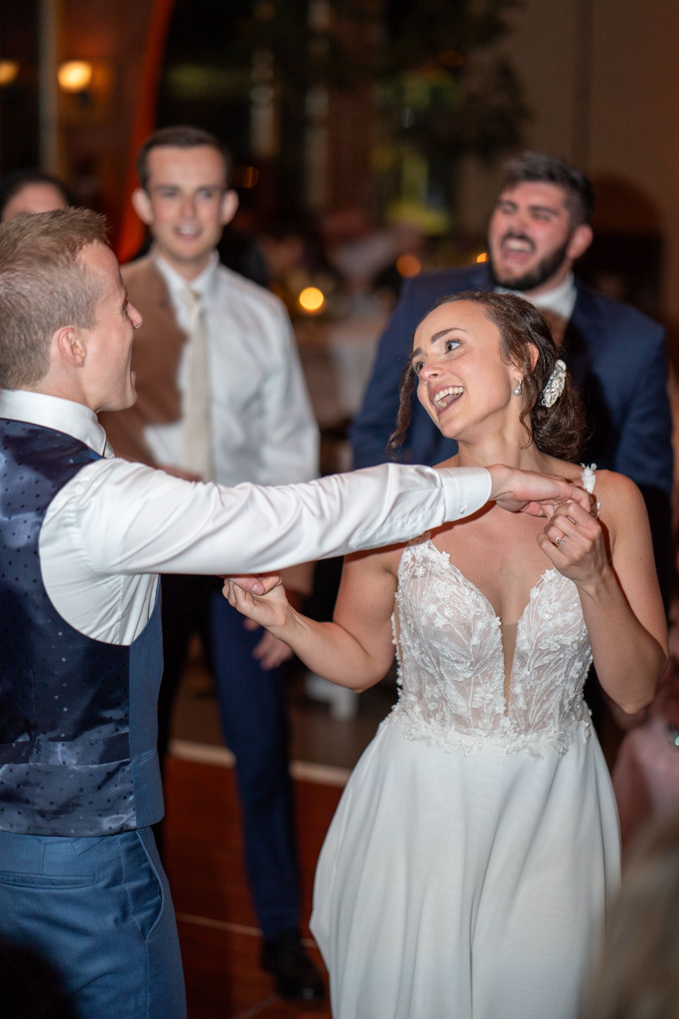 Couple dances energetically at wedding reception while guests look on.