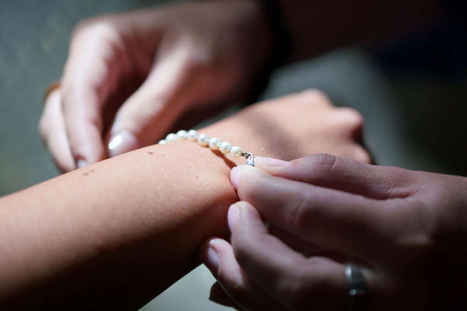 Closeup of hands fastening a delicate pearl bracelet around a wrist in soft natural lighting.