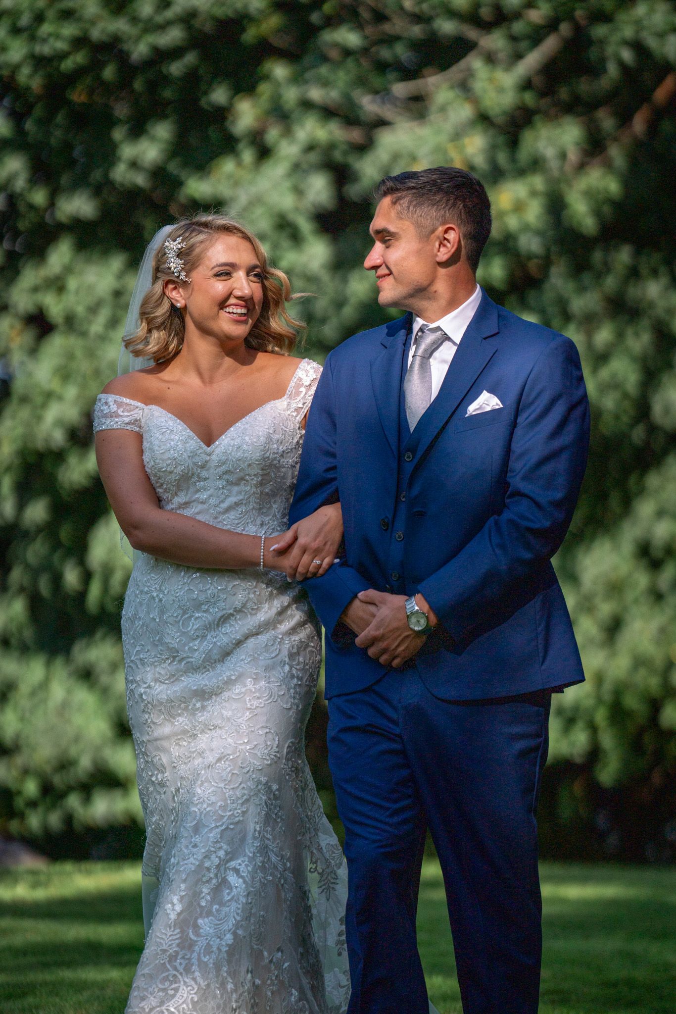 Couple in wedding attire share a happy moment in front of lush garden backdrop.