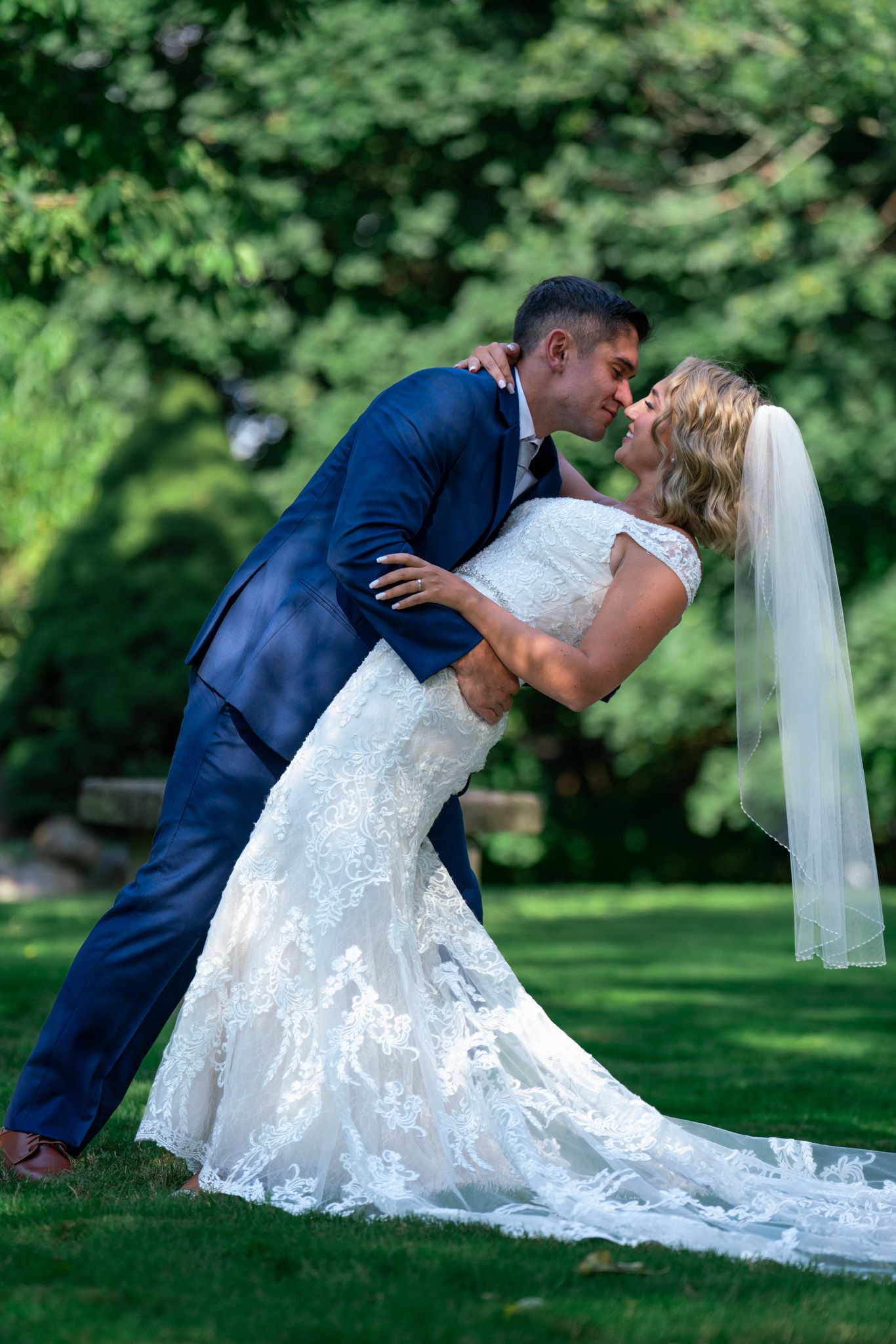 Couple performs romantic dip kiss pose on their wedding day in garden setting.