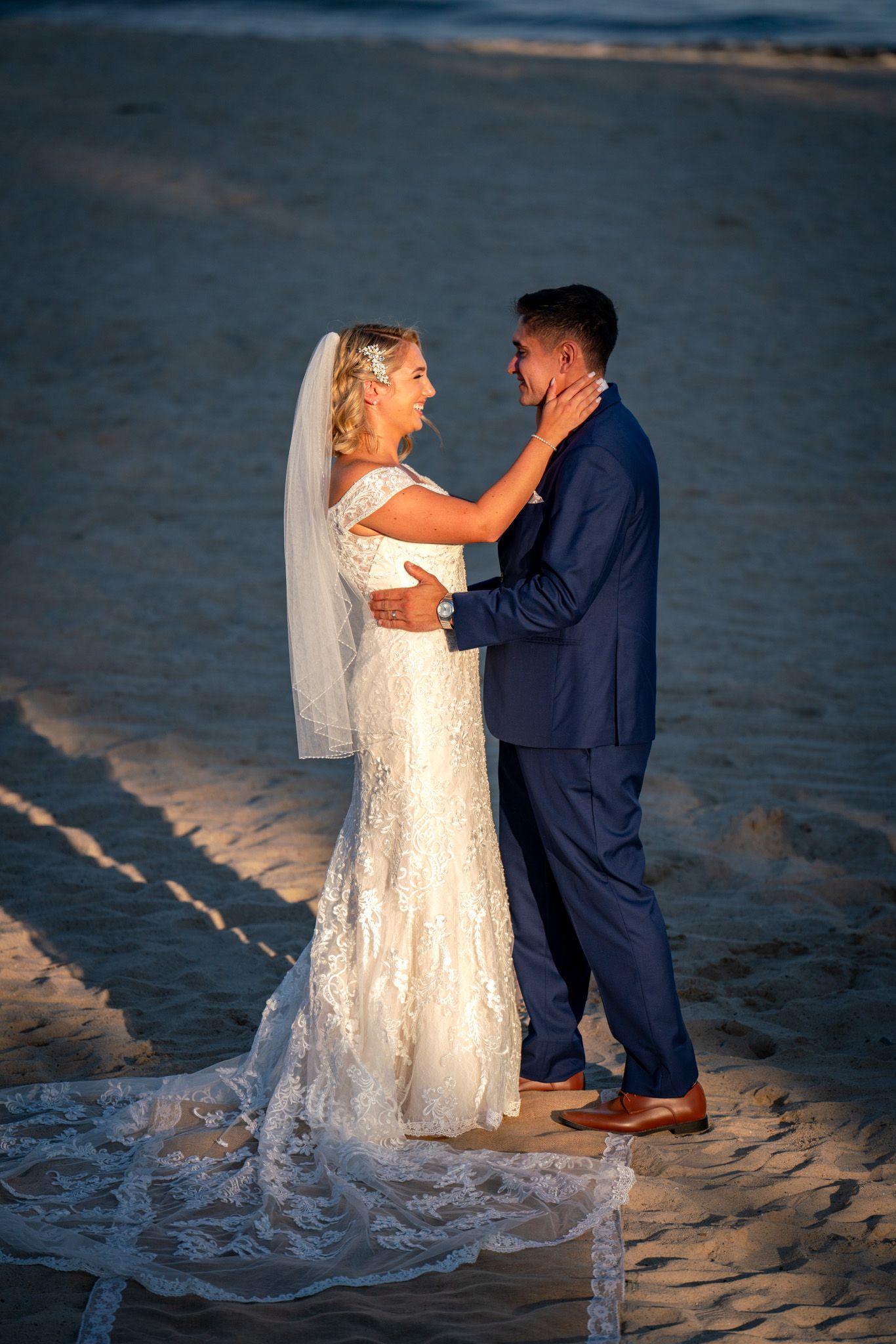 A romantic moment between newlyweds on a sandy beach at golden hour with flowing white wedding dress.
