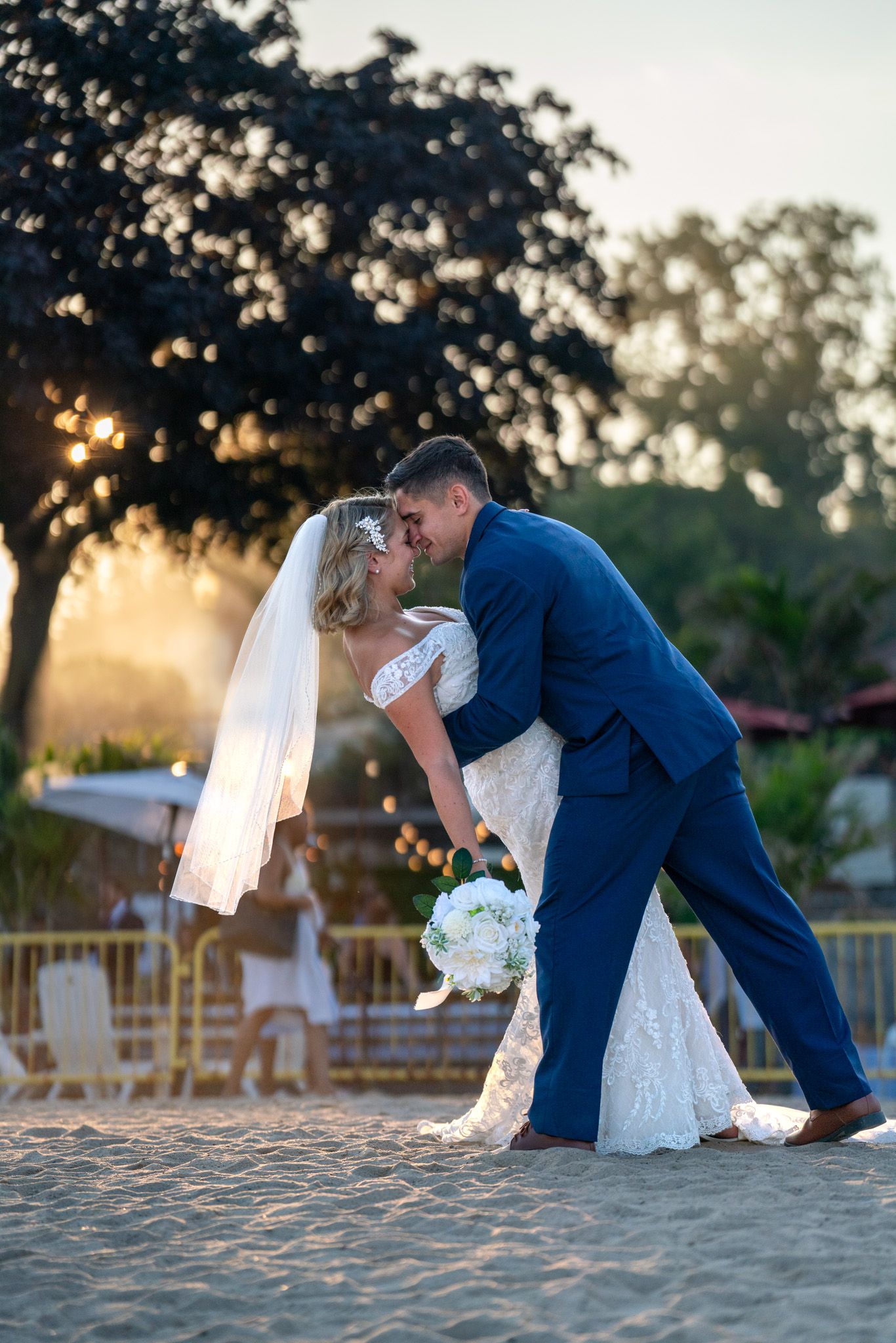 Romantic sunset wedding photo shows couple in a dramatic dip pose on the beach with golden light.