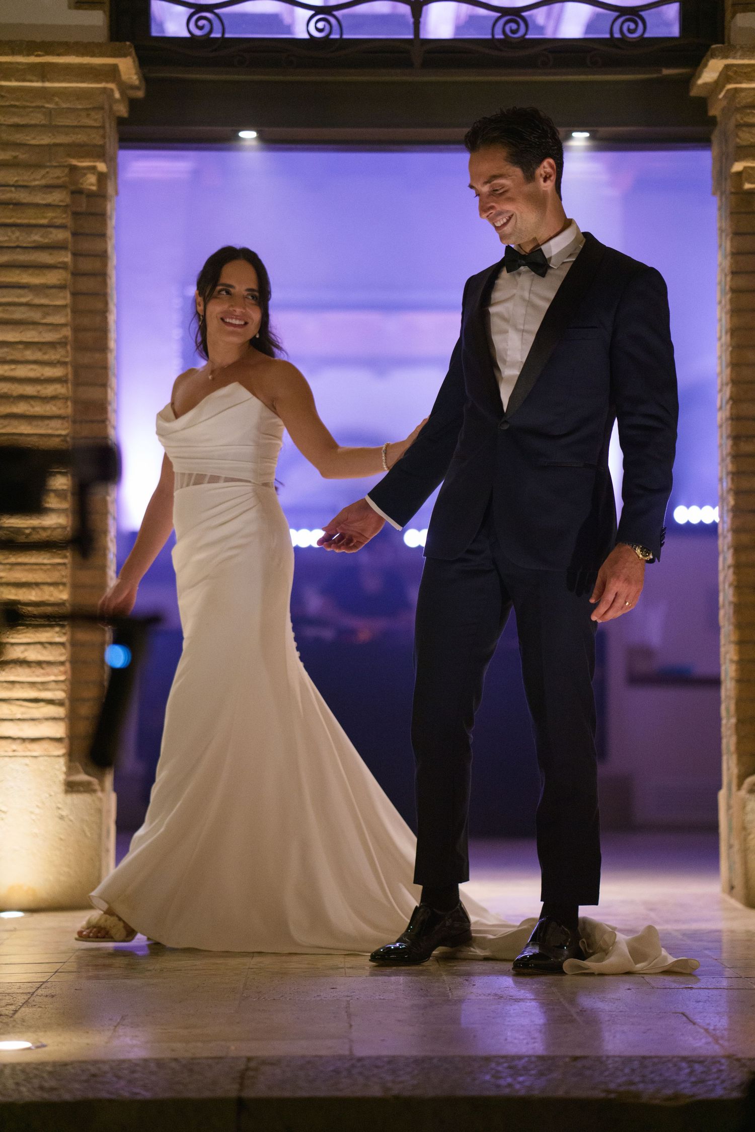 A couple in wedding attire shares a joyful moment while dancing in an elegantly lit venue.