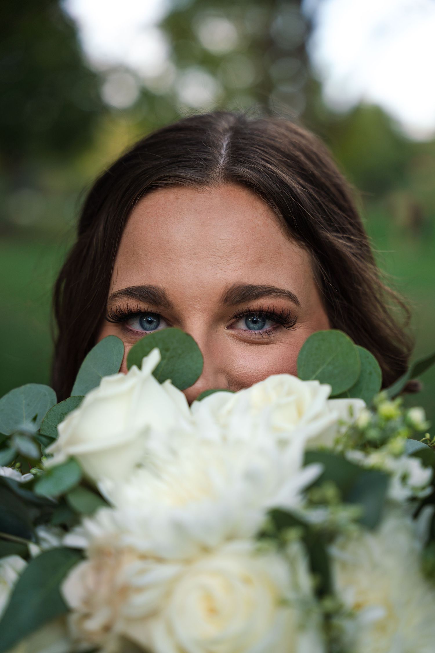 White roses and eucalyptus frame a close-up portrait peeking over a bridal bouquet.