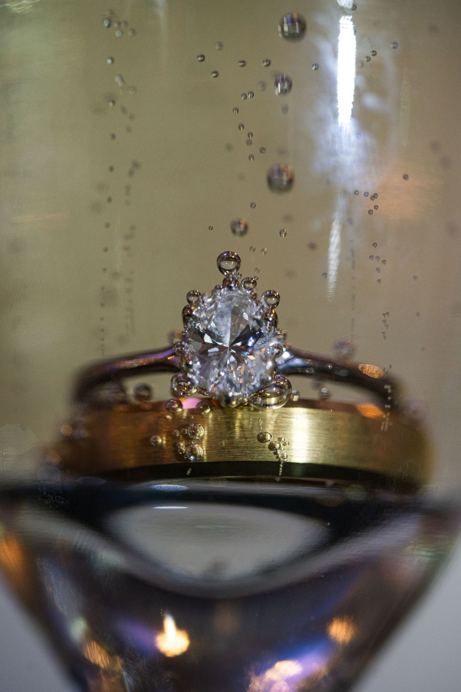 Sparkling diamond engagement ring photographed through champagne glass with bubbles.