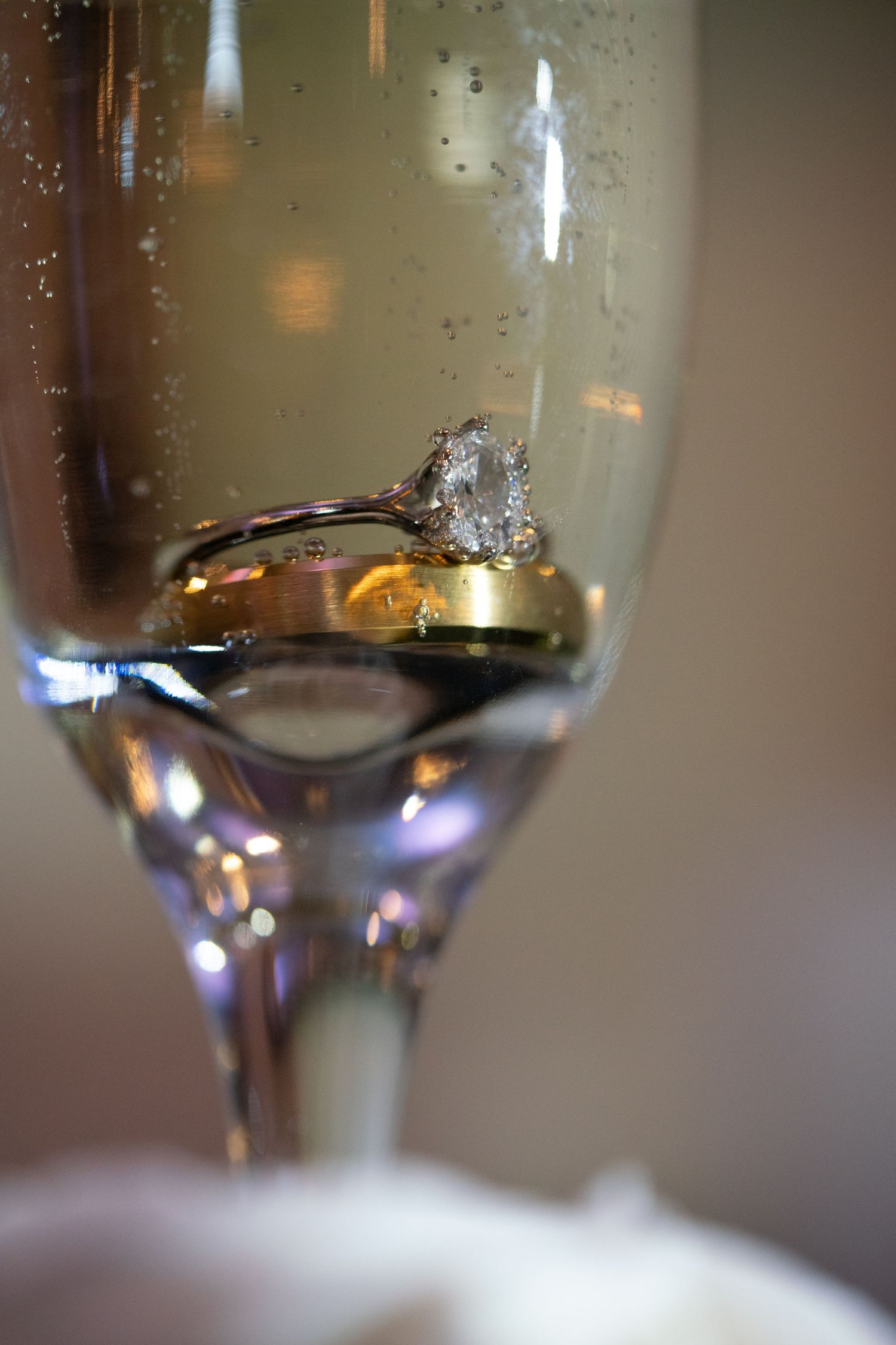 Diamond engagement ring and wedding band reflected in champagne glass with bubbles.