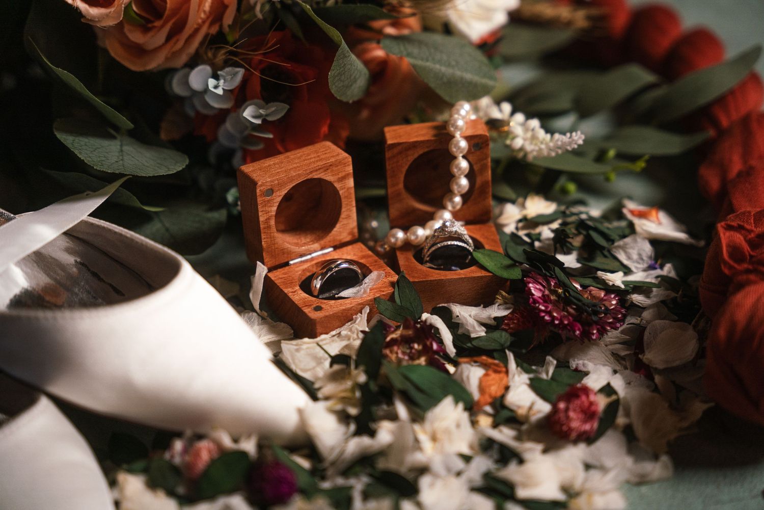 Wooden ring boxes nestled among red roses and white flowers with decorative greenery.