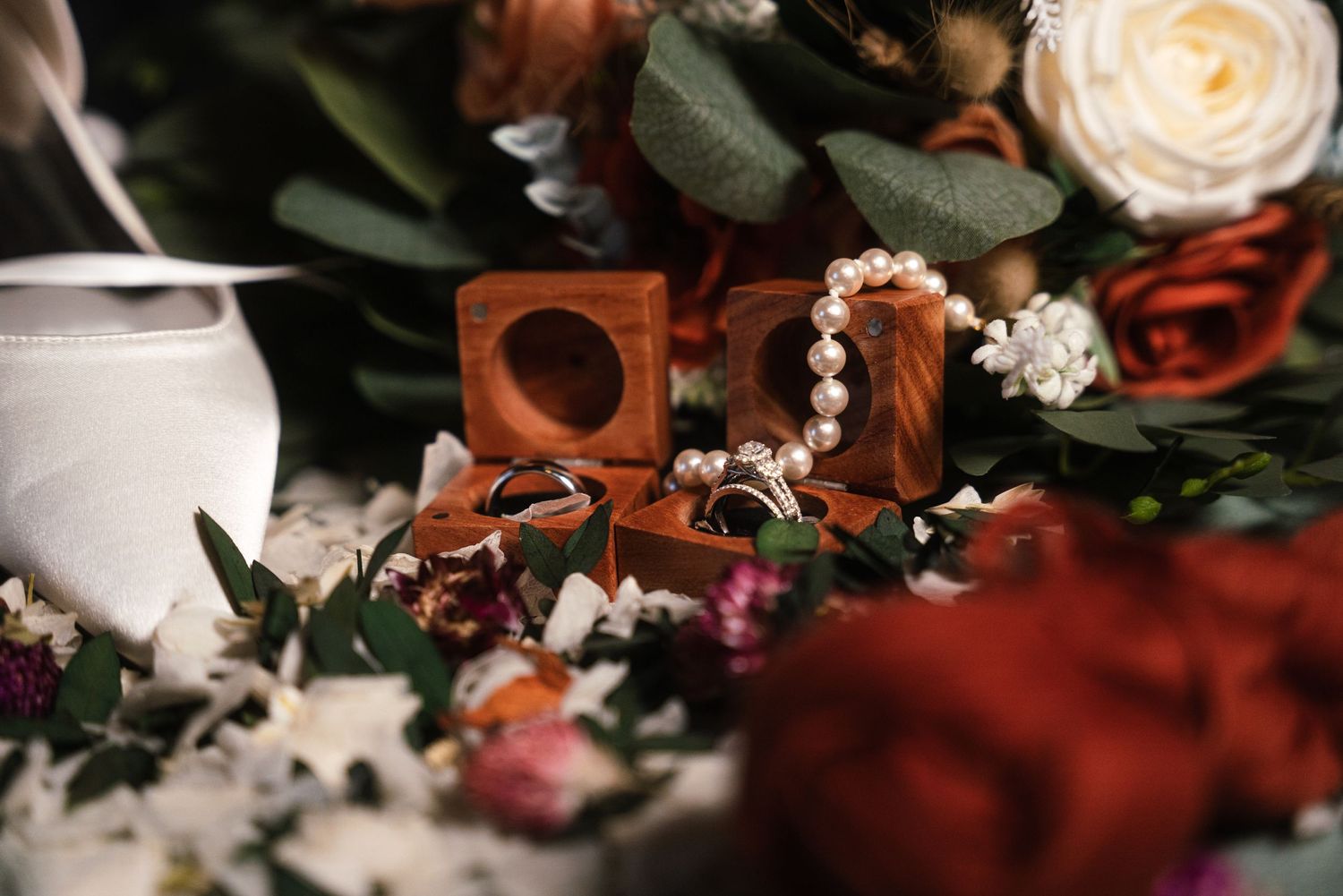 Wedding rings and jewelry arranged among delicate flowers and eucalyptus leaves in romantic lighting.