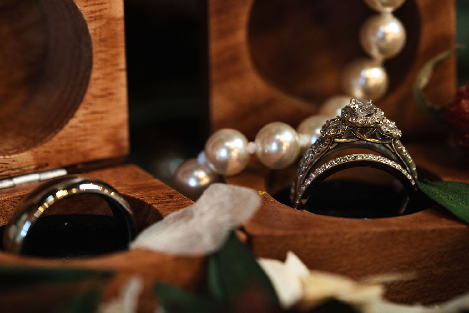 Close-up of diamond engagement rings and pearl jewelry displayed in a wooden box.