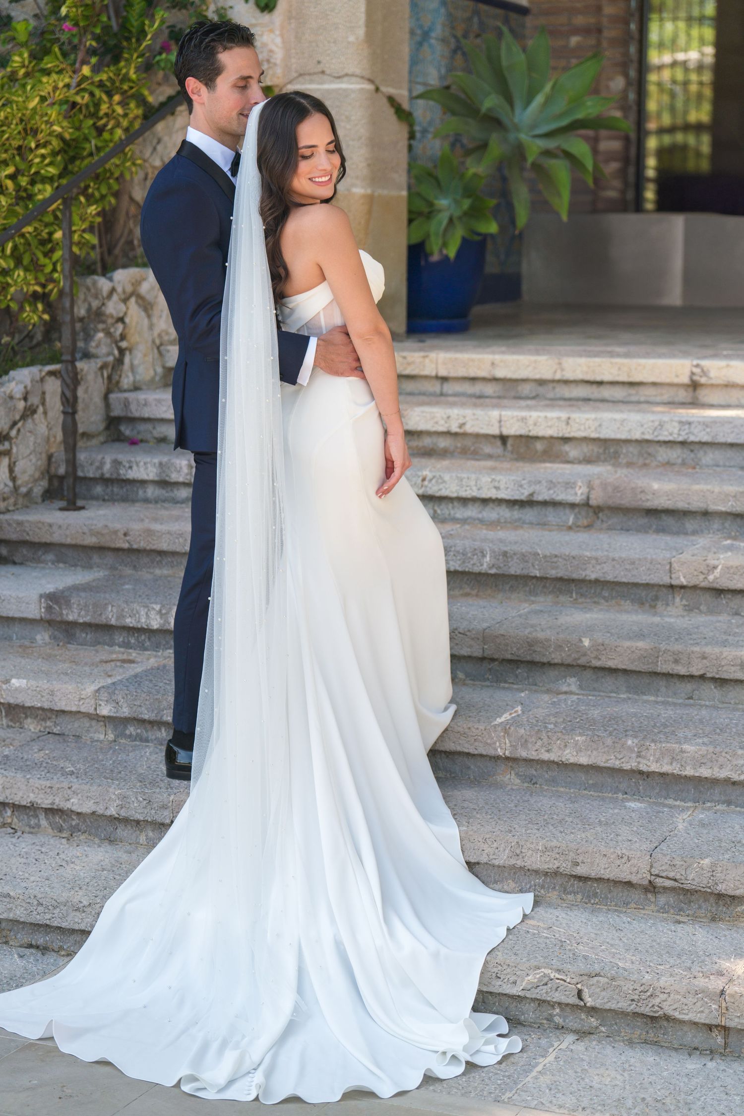 A stunning wedding dress with a flowing train cascades down outdoor stone steps.