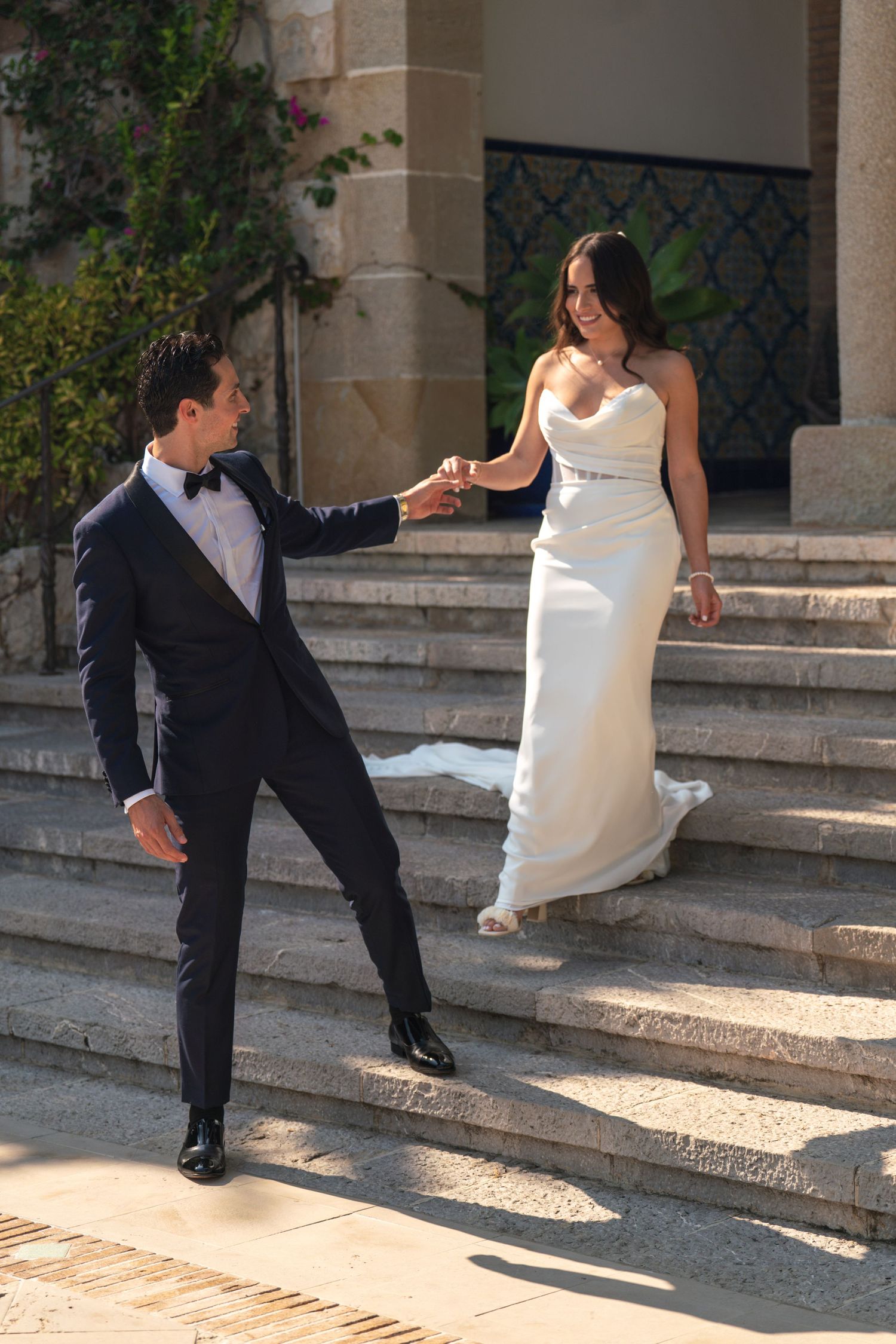 A playful moment between newlyweds on elegant stone steps in the sunlight.