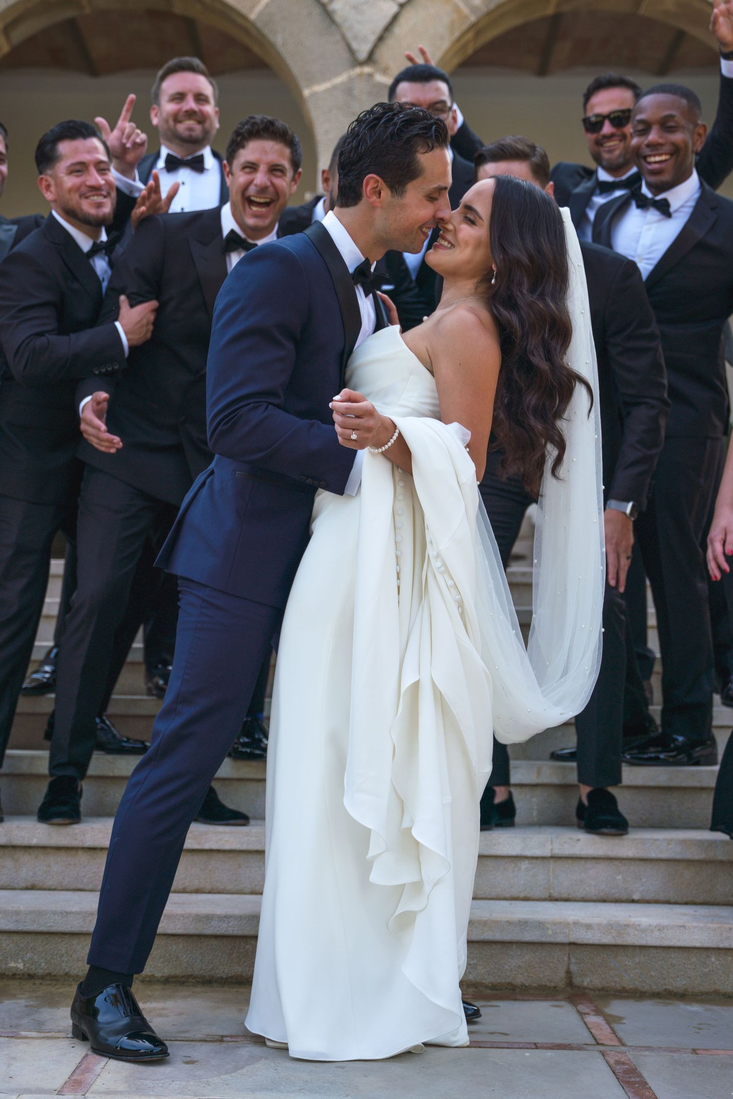 Wedding party celebrates with the newlyweds on stone steps at an elegant venue.