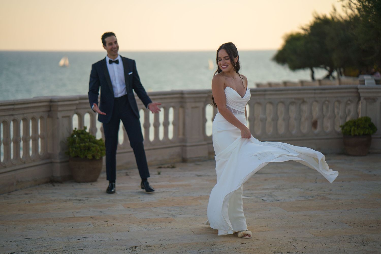 Playful wedding moment captured on coastal terrace as bride's dress catches the ocean breeze.