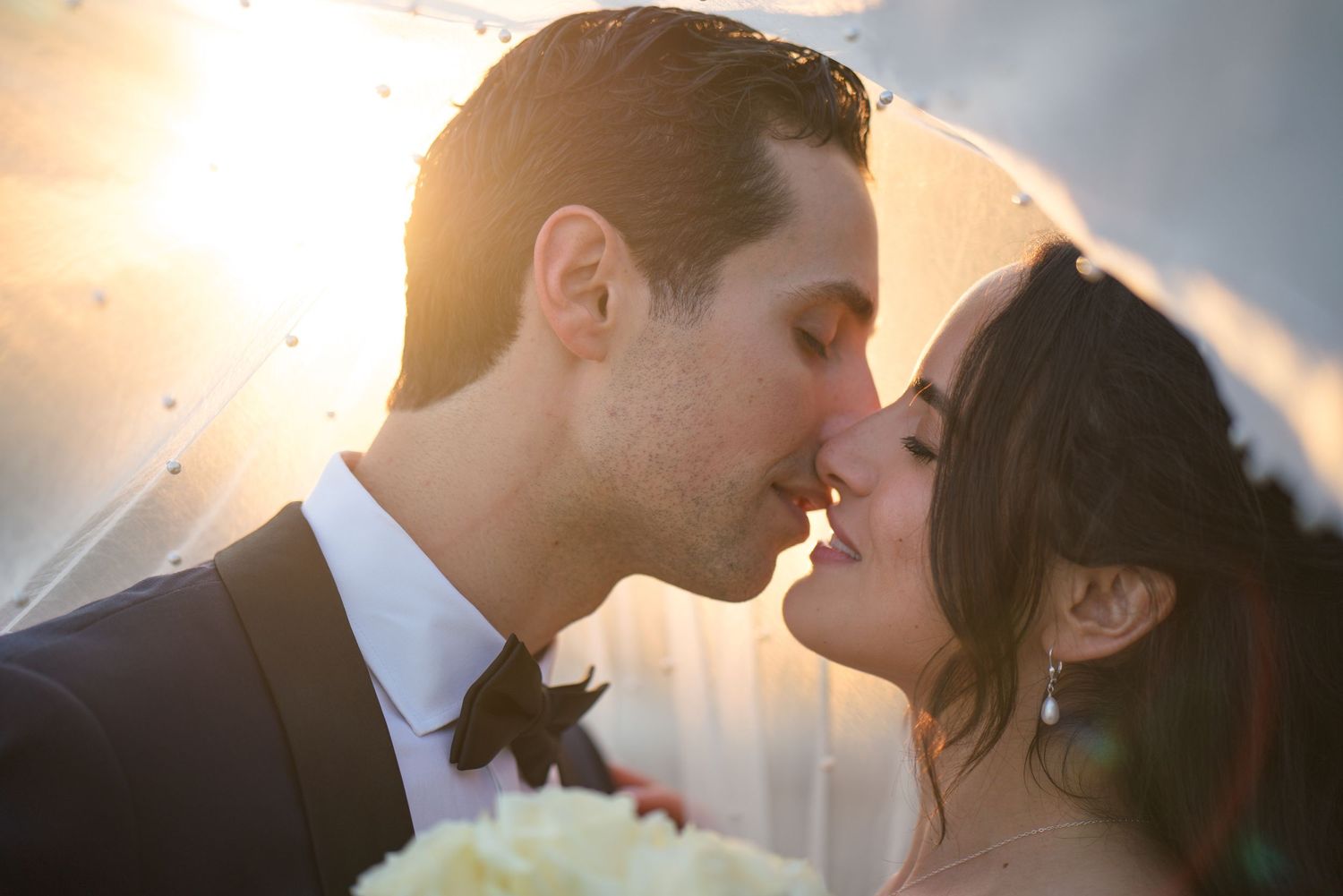 A romantic sunset kiss between newlyweds with golden backlighting.