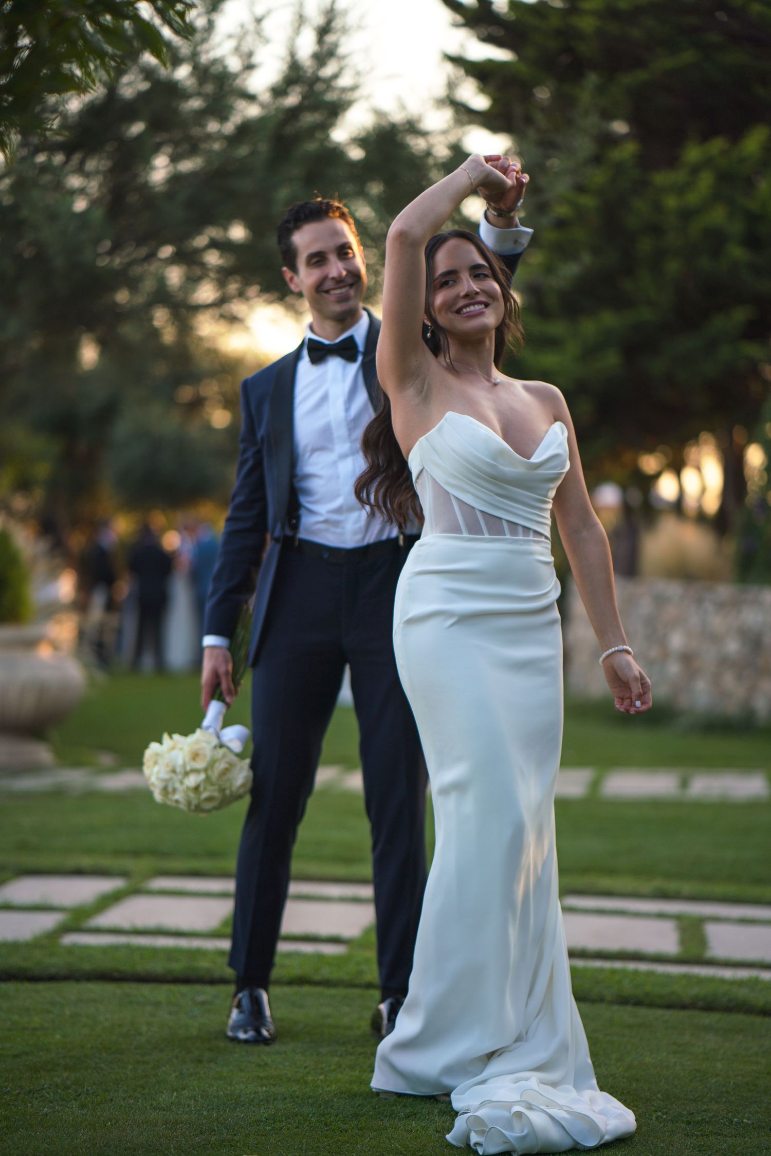 Dancing couple on manicured lawn during sunset wedding reception.