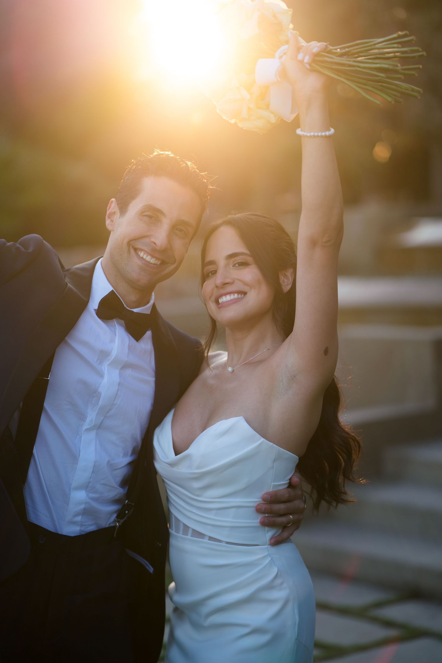 Joyful sunset celebration with bride holding bouquet high in the air.