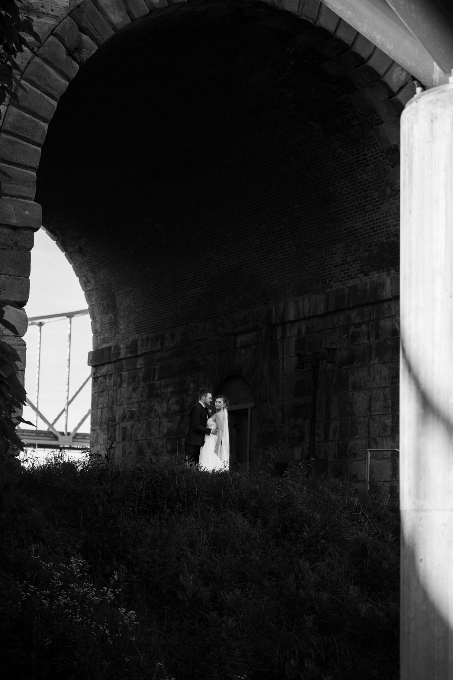 A silhouetted figure stands beneath a dark stone archway in a dramatic black and white composition.