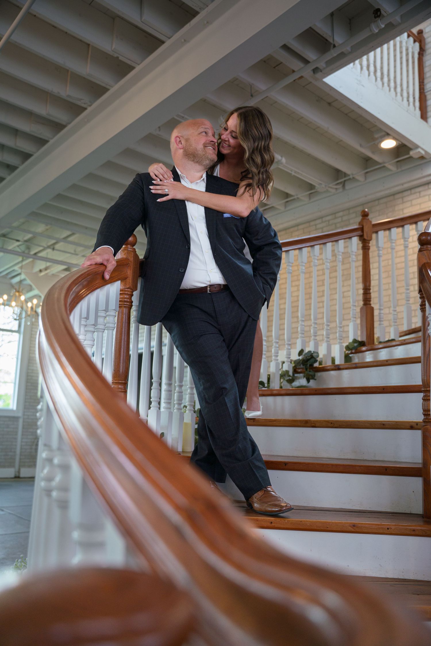 A romantic wedding photo captured on wooden stairs with a curved wooden banister in the foreground.