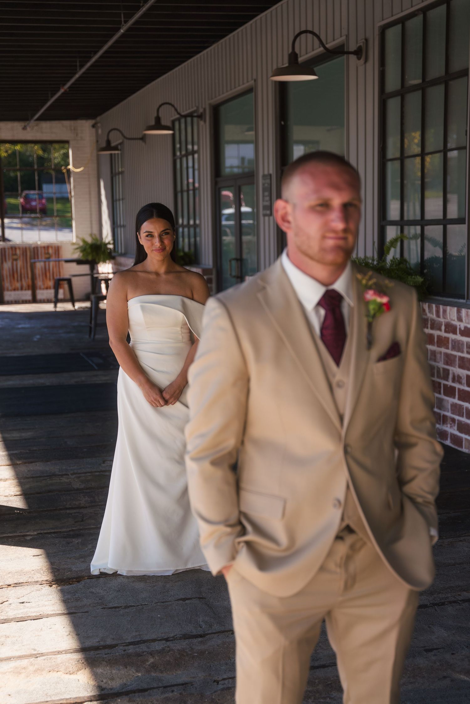 A first look wedding moment captured on a covered porch with brick walls and natural lighting.