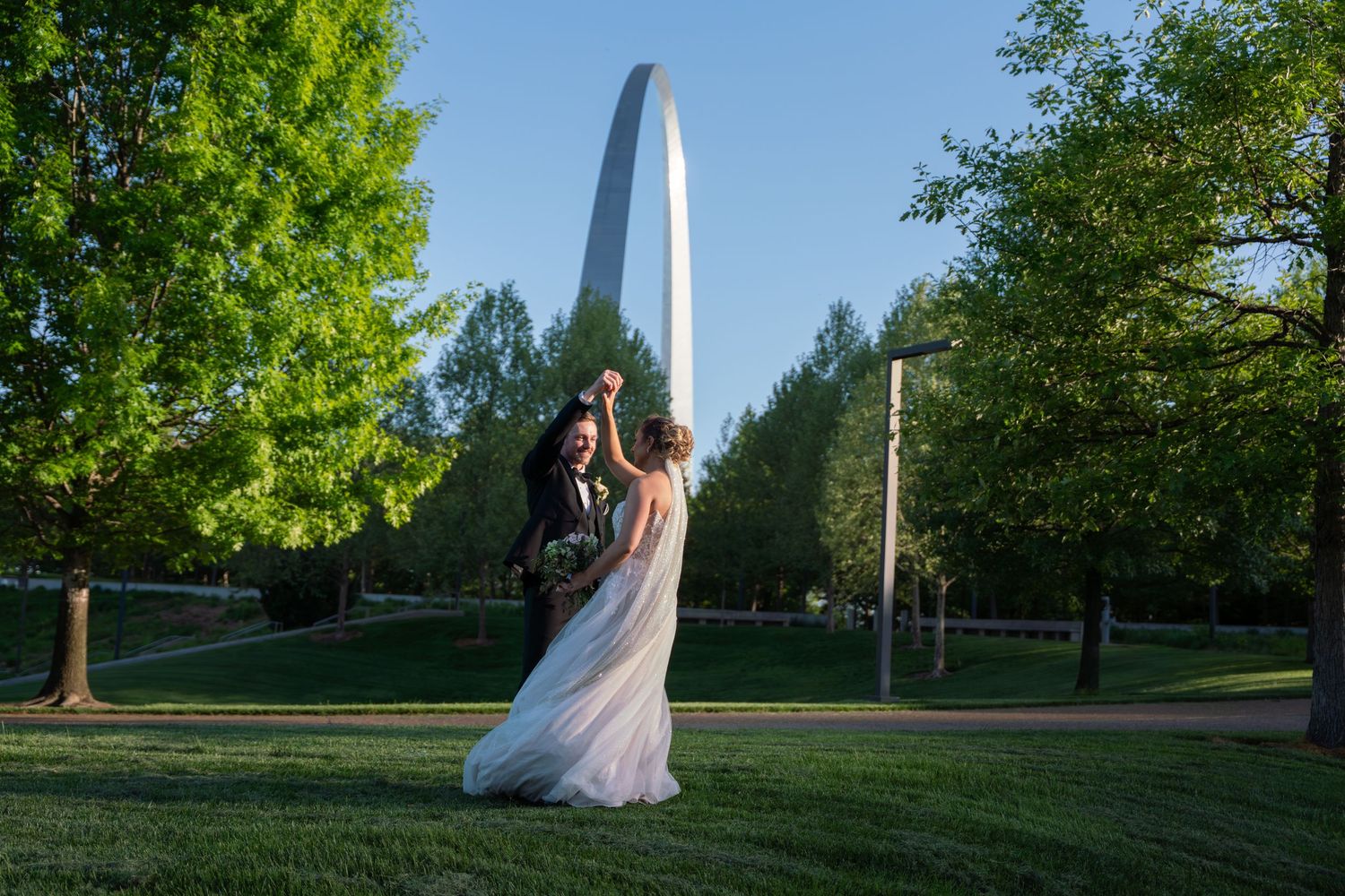 A couple shares an intimate dance on a green lawn with the Gateway Arch monument visible in the background in St. Louis.