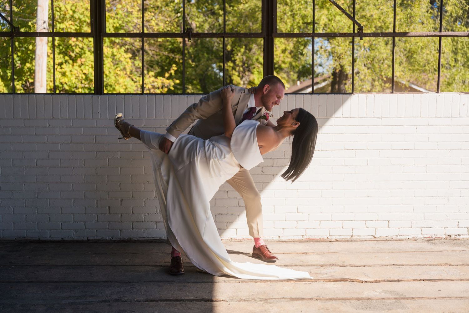 A romantic wedding dance dip pose captured in front of industrial windows.