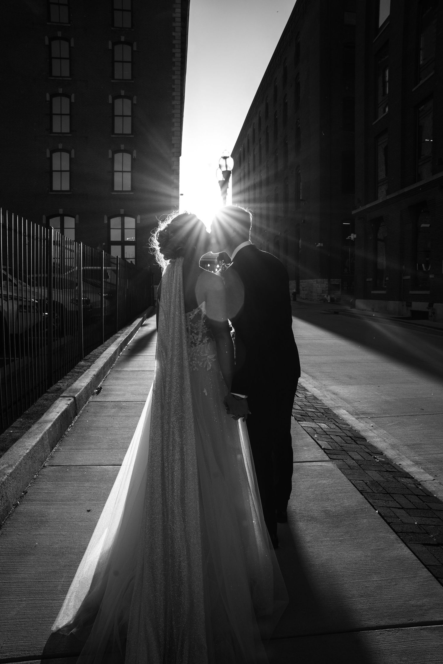 A romantic silhouette of a bride and groom embracing on a city street with sunlight creating a dramatic backlit effect.
