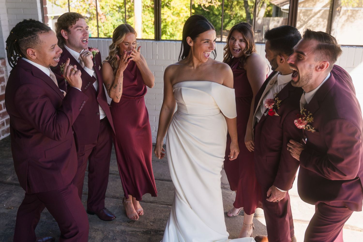 Wedding party in burgundy attire sharing a candid moment during group photos.