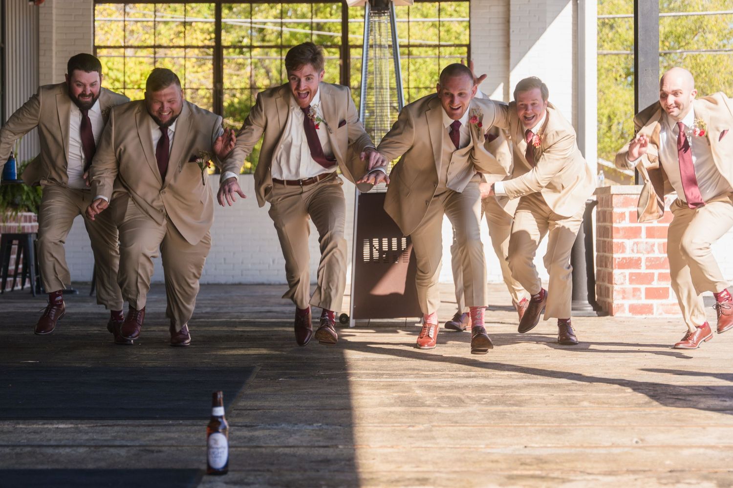 Groomsmen in tan suits running playfully down a covered porch during wedding photos.