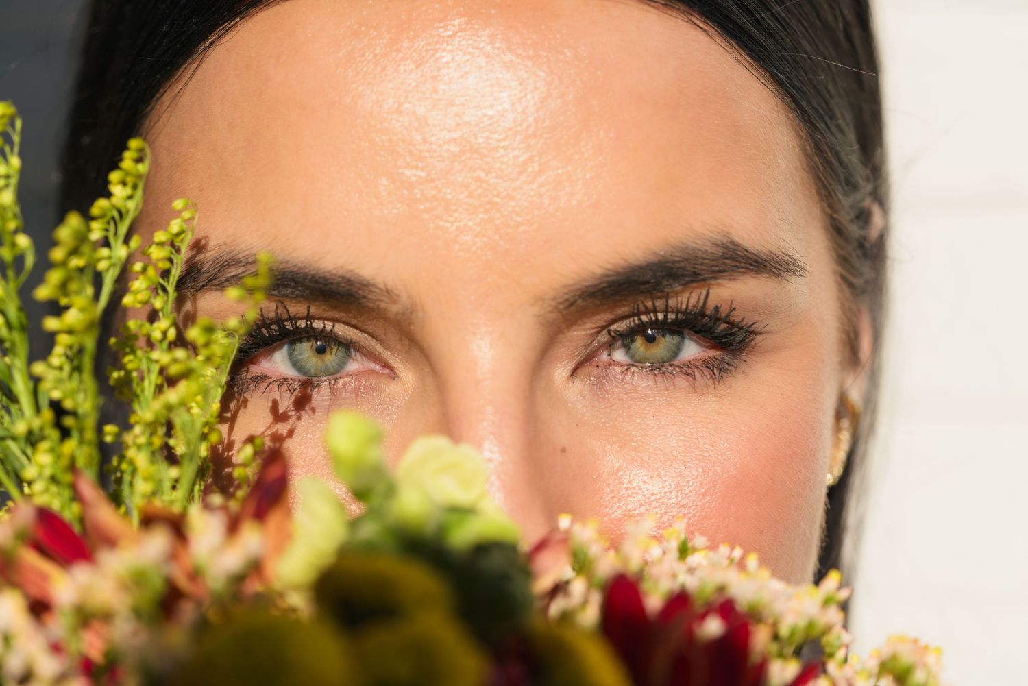 Close up beauty shot of eyes peeking over a wedding bouquet with natural greenery.