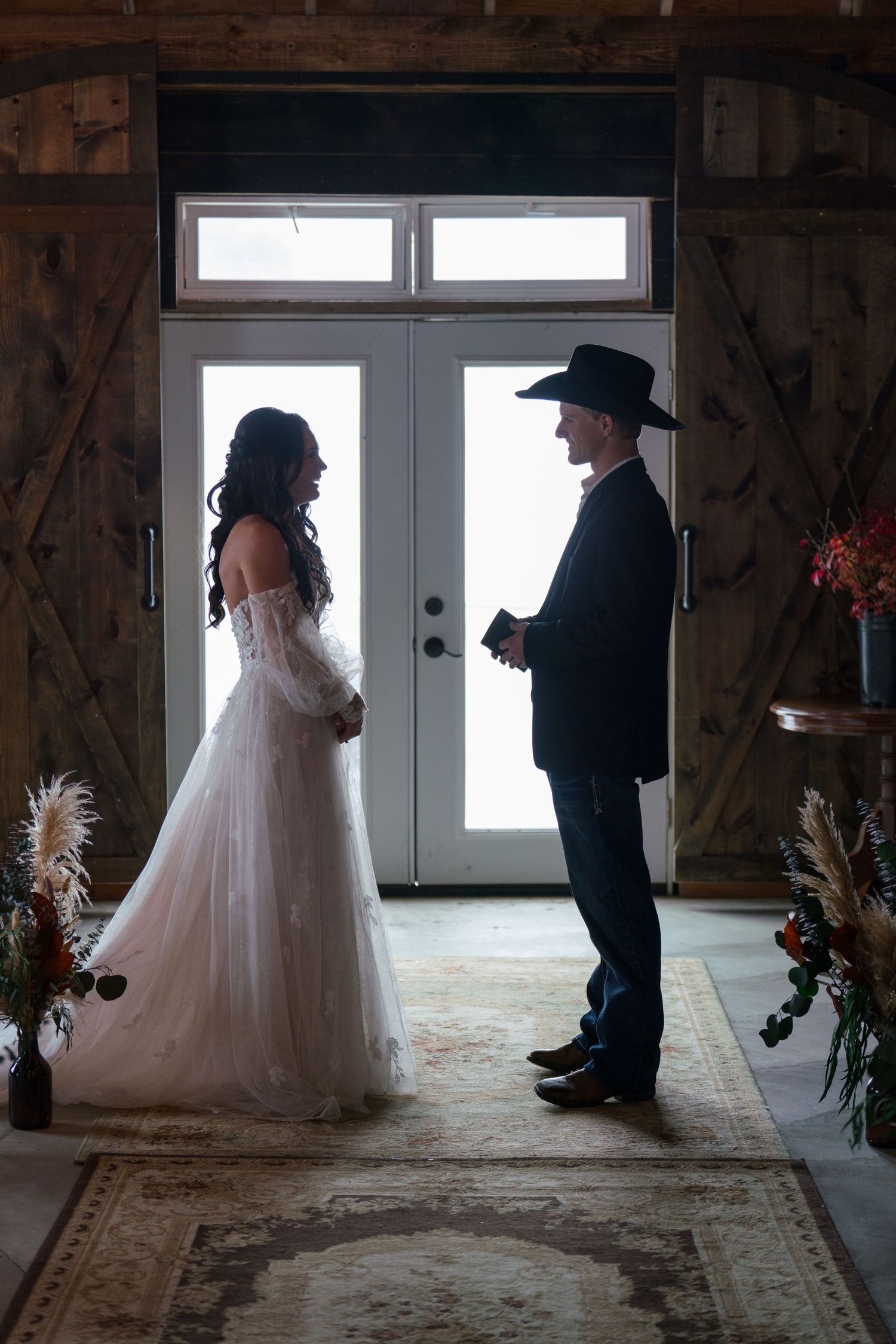 A silhouetted wedding moment against bright doorway windows in a rustic barn setting.