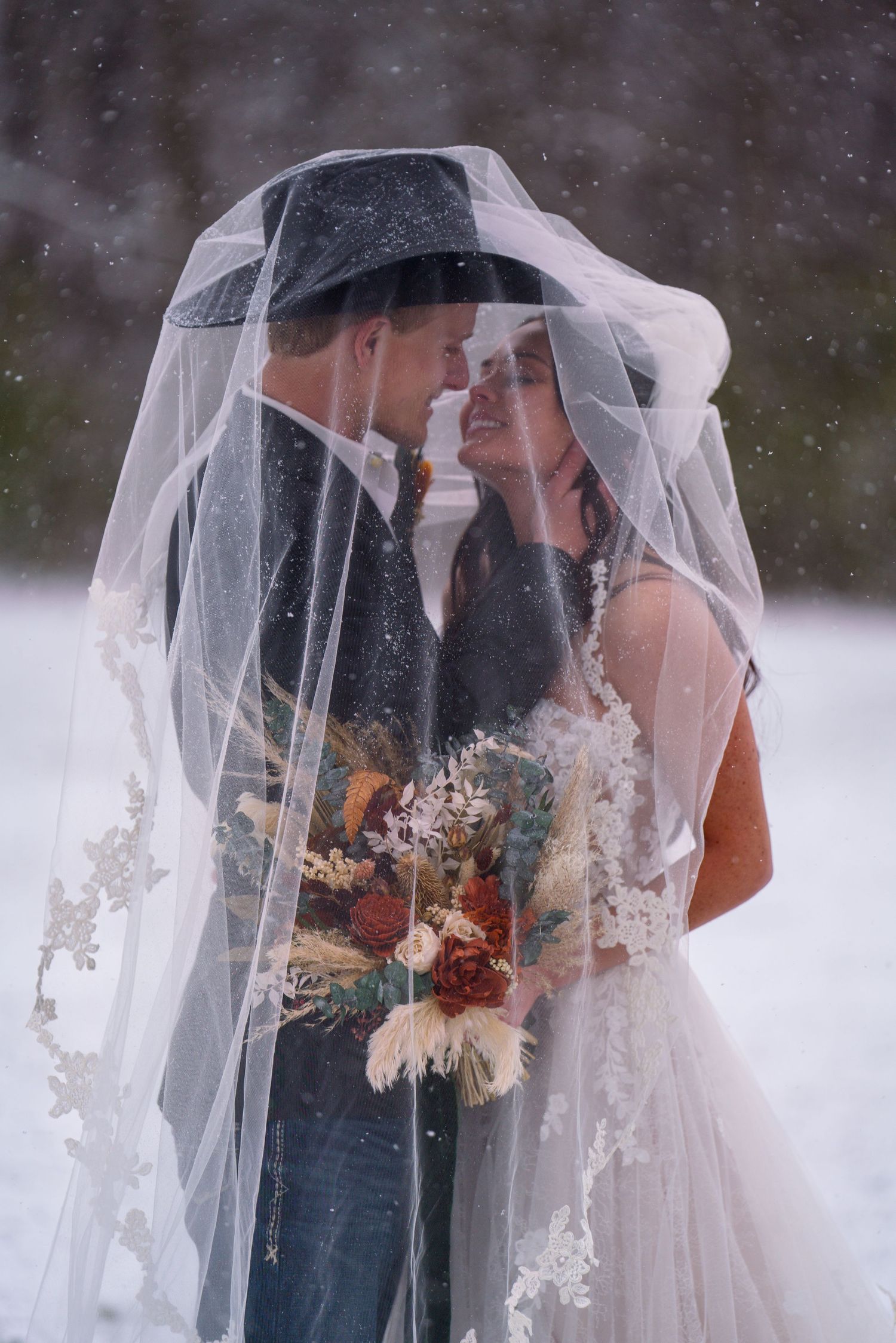 An intimate winter wedding moment under a delicate veil with snowflakes falling in the background.