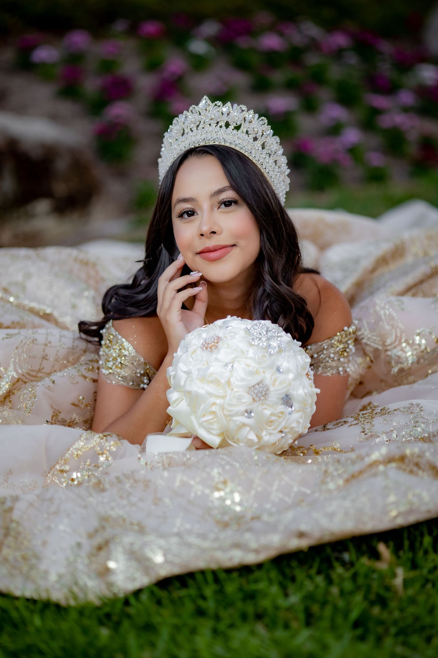 Young woman in gold quinceañera gown wearing crystal crown holding white floral bouquet.