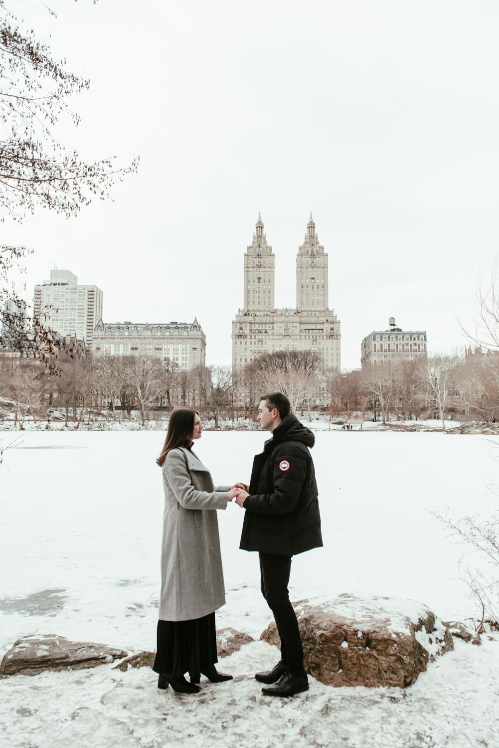 Winter engagement photos with snowy Central Park and NYC buildings in background.